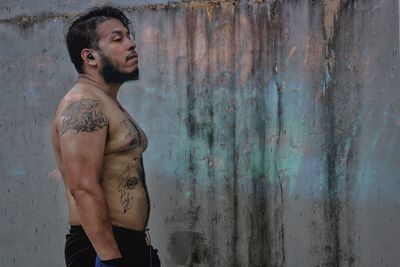 Side view of young man looking away against wall