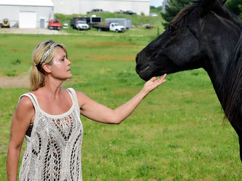 Woman touching horse while standing on grassy field