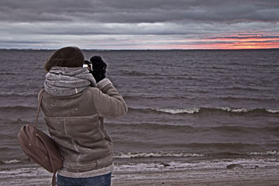 Rear view of woman photographing sea against sky