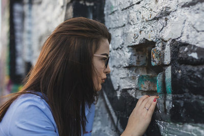 Side view of young woman looking through hole in wall
