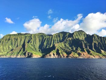 Scenic view of sea and green mountains against blue sky