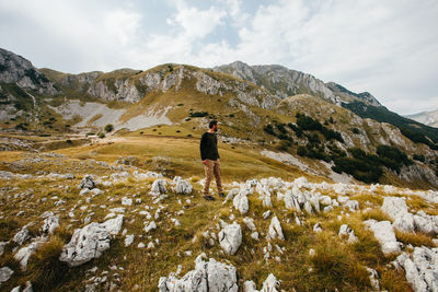 A young man hiker with beard is standing on rocky cliff with green autumn grass. mountain landscape