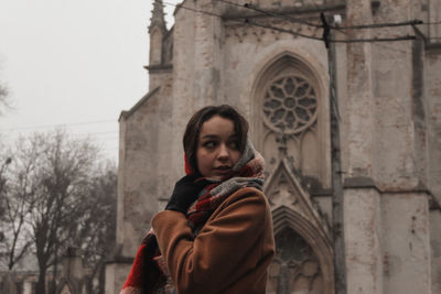 Portrait of woman standing in snow against building 