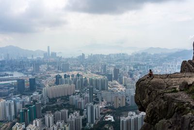 Man sitting on rock against cityscape