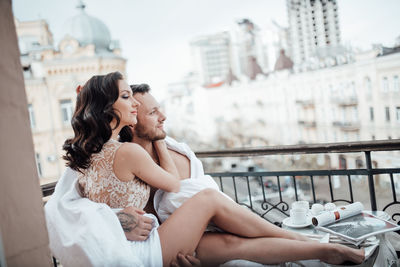 Friends sitting on bridge against buildings
