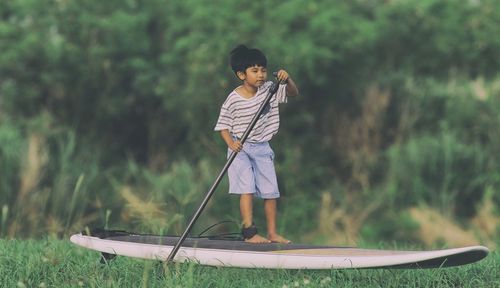 Cute boy standing on paddleboard against trees