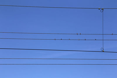 Low angle view of power lines against clear blue sky