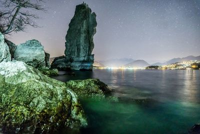 Rock formation by sea against sky at night