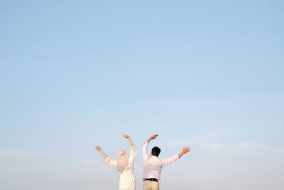 Rear view of woman with arms raised against clear sky