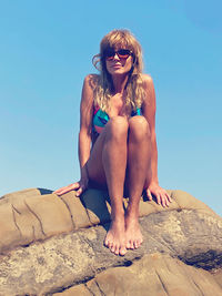 Low angle view of woman sitting on rock against sky