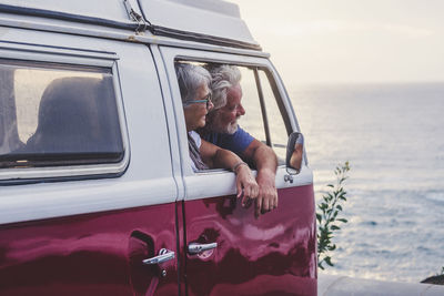 Senior couple traveling in a vintage van, looking at the sea