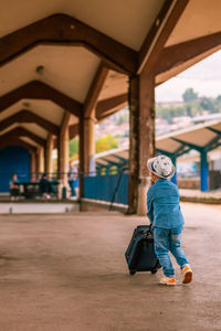 Rear view of boy holding suitcase standing on railroad station platform