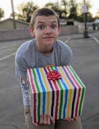 Portrait of a boy holding a large rainbow striped gift box