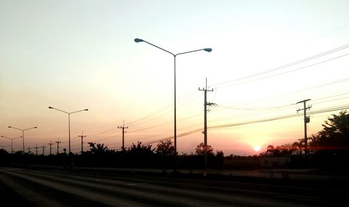 Silhouette street lights against sky during sunset