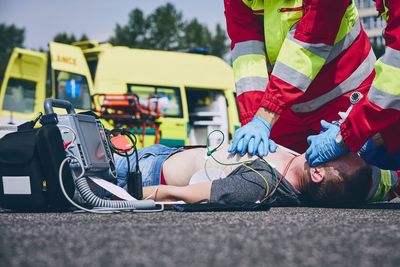 Midsection of paramedic giving cpr to unconscious man lying on street