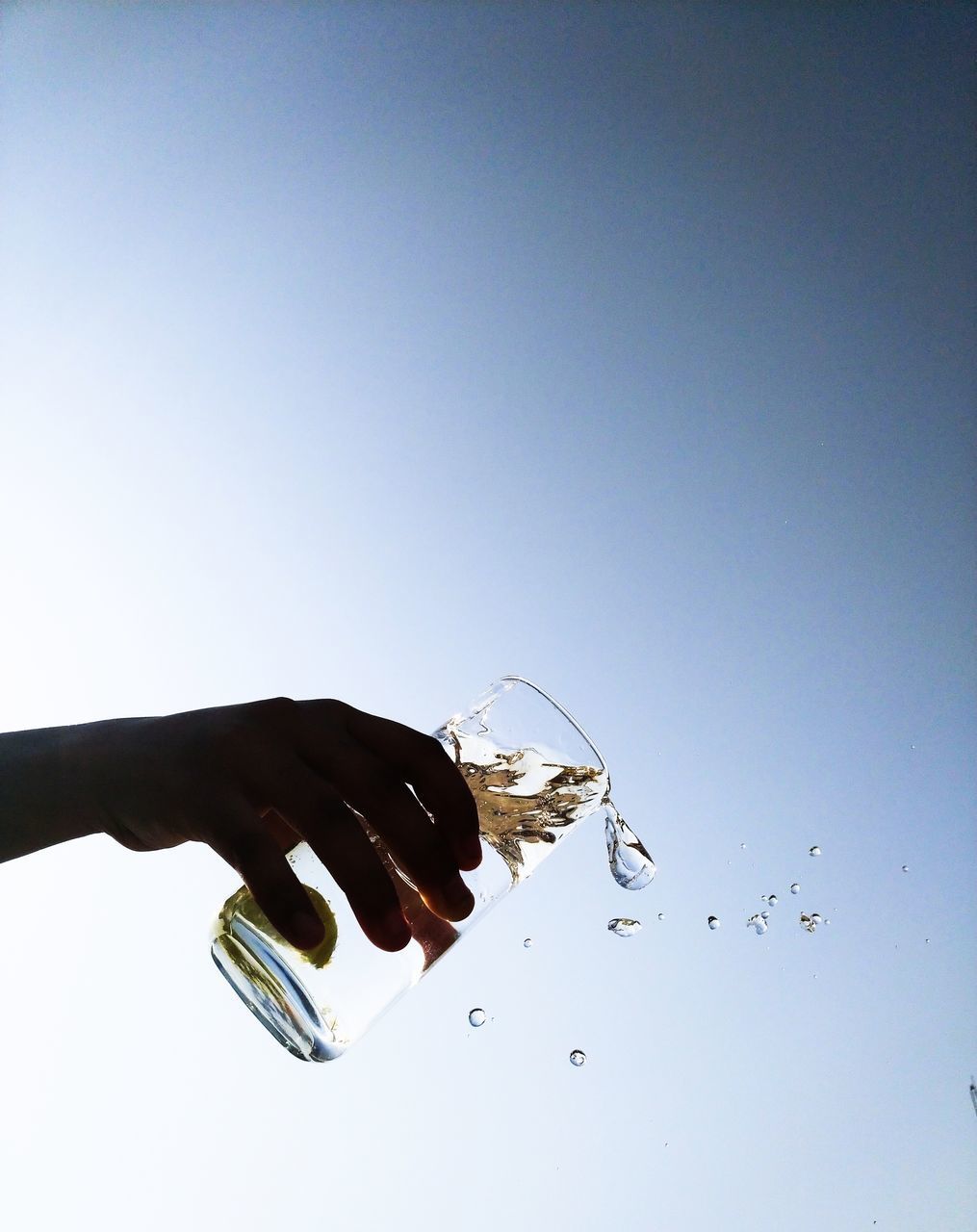 CLOSE-UP OF HAND HOLDING GLASS OVER WATER AGAINST SKY