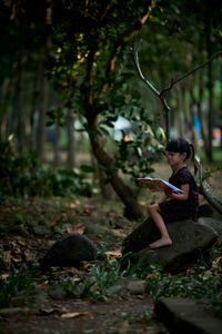 Little child reading a book in a green coastal forest