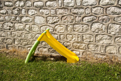 Small slide on grassy field against brick wall