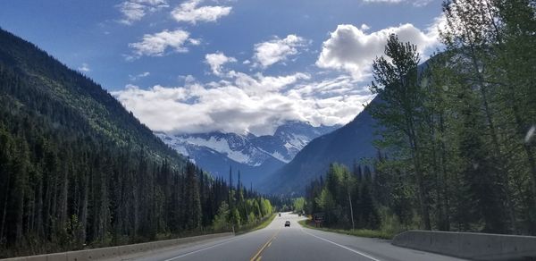 Road amidst trees and mountains against sky