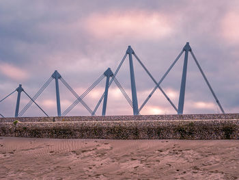 Steel cables and pillars of a bridge visible behind pier at the beach