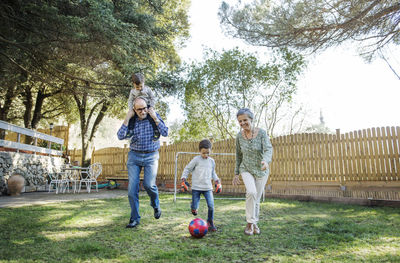 Full length of grandparents and grandsons playing soccer at yard