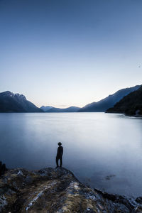 Man standing on rock by lake against sky