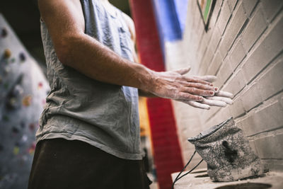 Midsection of sportsperson chalking hands while standing at gym