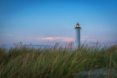 Lighthouse by sea against sky during sunset