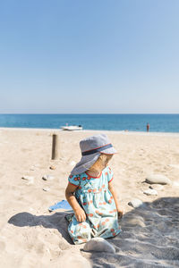 Girl sitting on sand at beach against clear sky