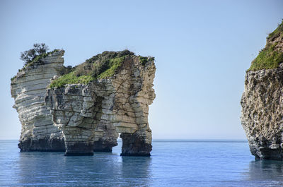 Rock formations in sea against clear sky