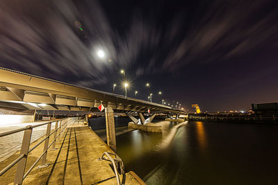 Low angle view of illuminated bridge over river against sky at night