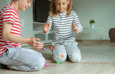 Cheerful siblings playing with dice while sitting on carpet at home