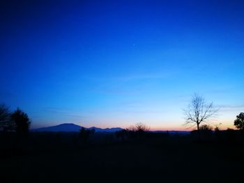 Silhouette landscape against clear blue sky at night