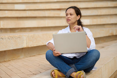 Young woman using laptop while sitting on steps