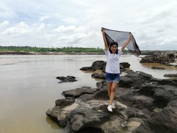 Full length of woman standing on rock at sea shore against sky