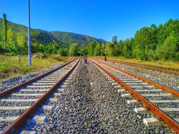 Railroad tracks by trees against clear blue sky