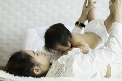 Smiling mother playing with daughter while lying on bed at home