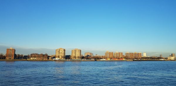 Sea by buildings against clear blue sky