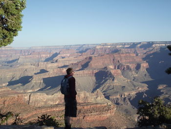 Full length of hiker standing on cliff against rocky mountains at grand canyon national park
