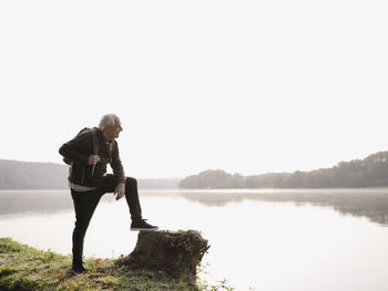 Senior man with backpack looking at view while standing by lake