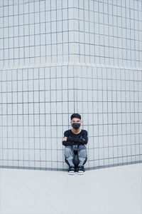 Portrait of young man sitting against wall