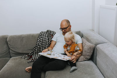 Father reading toddler book on sofa