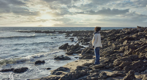 Man standing on rock by sea against sky