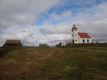 Church on field by buildings against sky