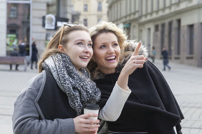 Happy young woman using mobile phone in city during winter