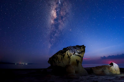 Rock formation at beach against star field at dusk