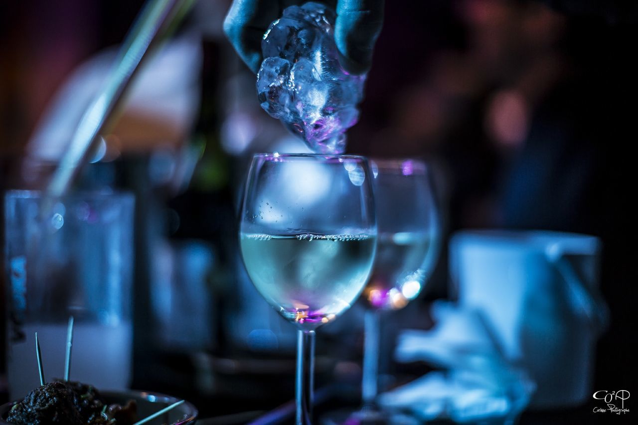 focus on foreground, close-up, glass - material, indoors, transparent, wineglass, illuminated, drinking glass, food and drink, wine, alcohol, drink, selective focus, celebration, night, lighting equipment, refreshment, glass, still life