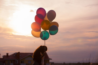 Man holding colorful balloons against sky during sunset