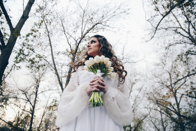 Low angle view of woman standing against trees and plants