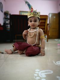 Cute boy in traditional clothing sitting on floor at home